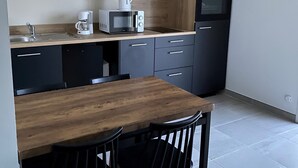 Ett modernt kök med svarta skåp, ett träbord, två svarta stolar, en kaffebryggare, en mikrovågsugn och en inbyggd ugn.