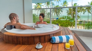 A couple relaxing in a hot tub with a view of the beach and palm trees.