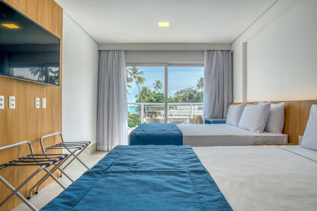 Een hotelkamer met twee bedden, een televisie en een balkon met uitzicht op palmbomen.