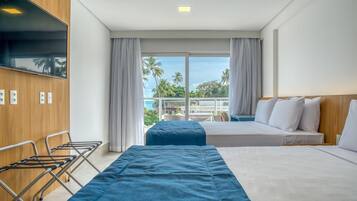 A hotel room with two beds, a TV, and a balcony with a view of palm trees.