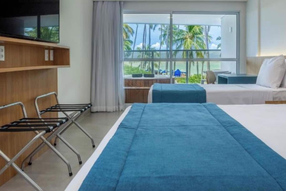 Een hotelkamer met een bed, een bureau en uitzicht op palmbomen en de oceaan.