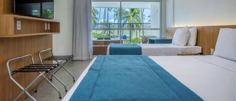 A hotel room with a bed, a desk, and a view of palm trees and the ocean.