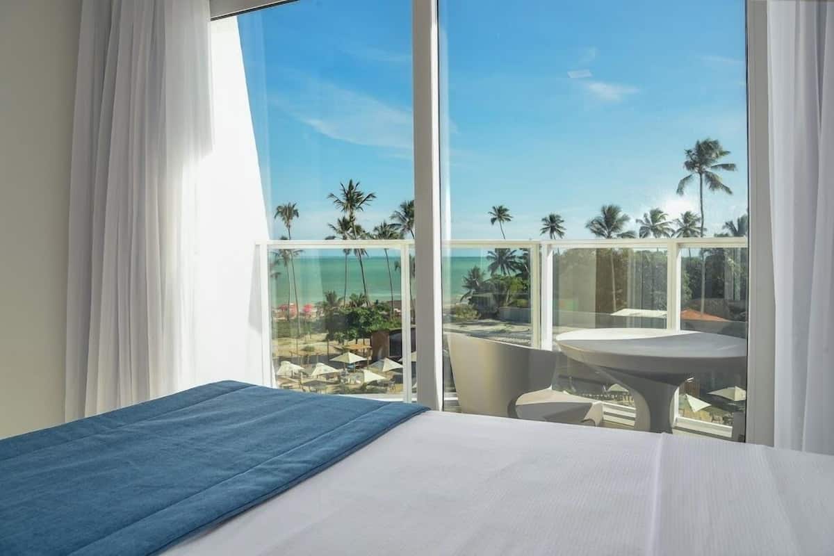 Een hotelkamer met een bed, een tafel en uitzicht op het strand en palmbomen.