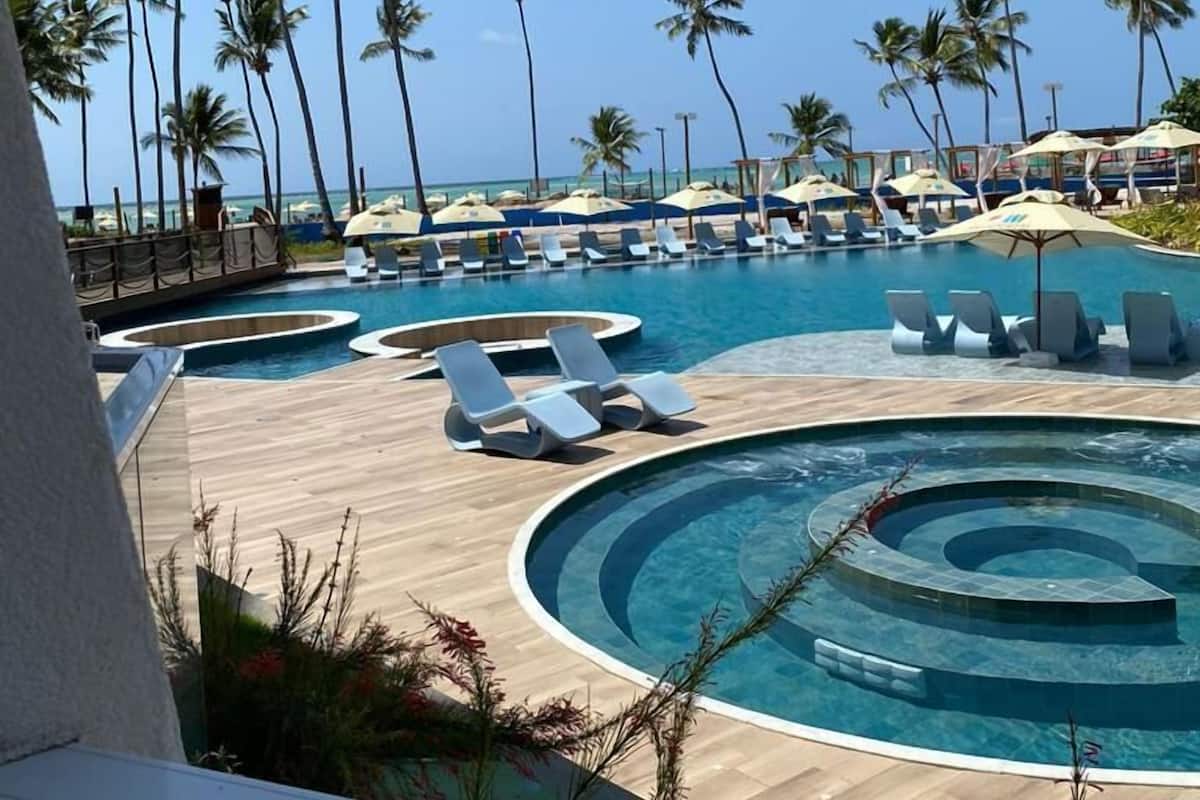 Een zwembadgedeelte van een resort met meerdere ligbedden en parasols, omringd door palmbomen.