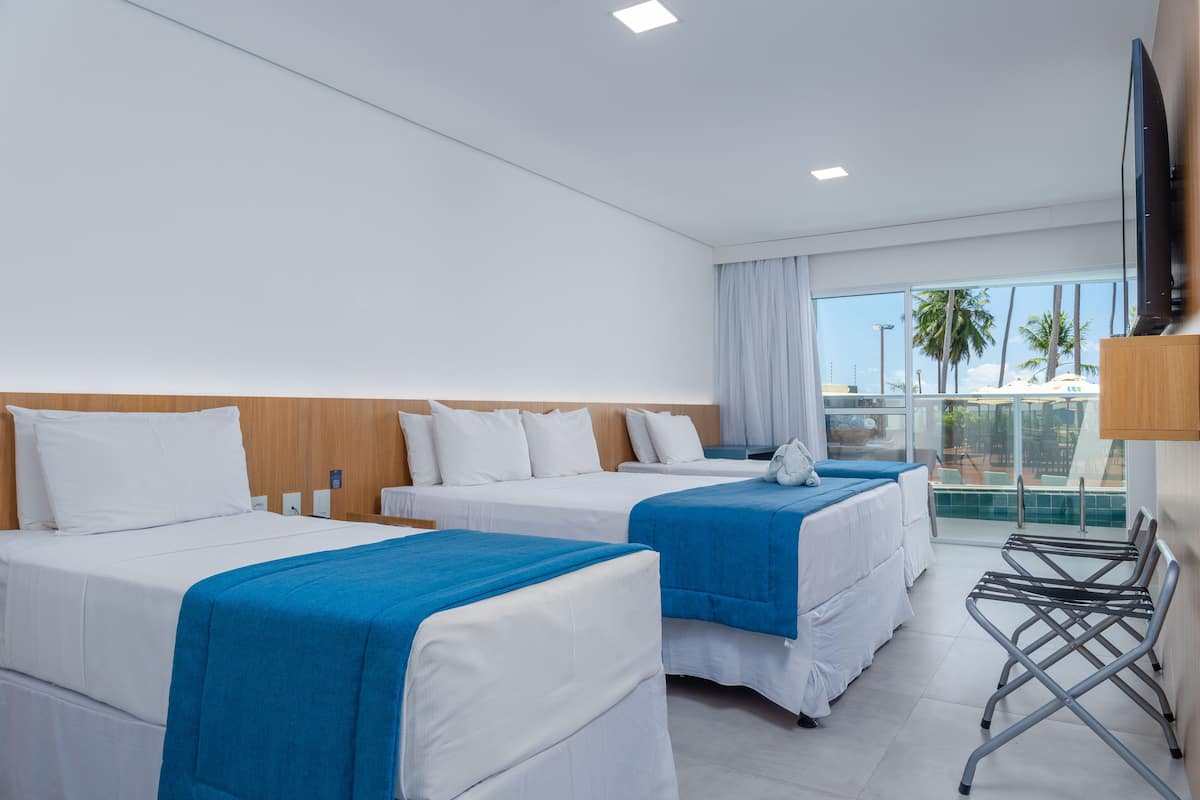 Een hotelkamer met twee bedden, een televisie en een balkon met uitzicht op palmbomen.