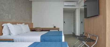 Una habitación de hotel con dos camas, un televisor montado en la pared y una zona de estar con sillones.