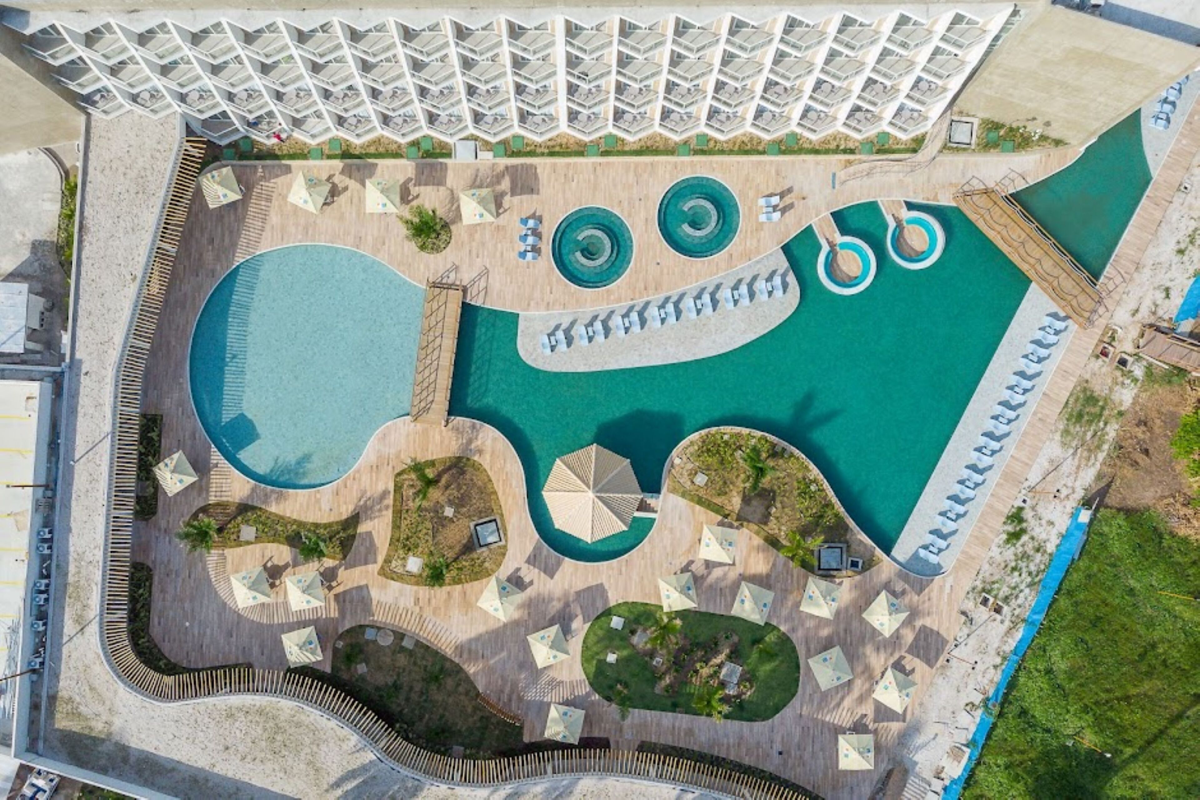 An aerial view of a resort with multiple swimming pools, sun loungers, and a large building with a unique roof design.