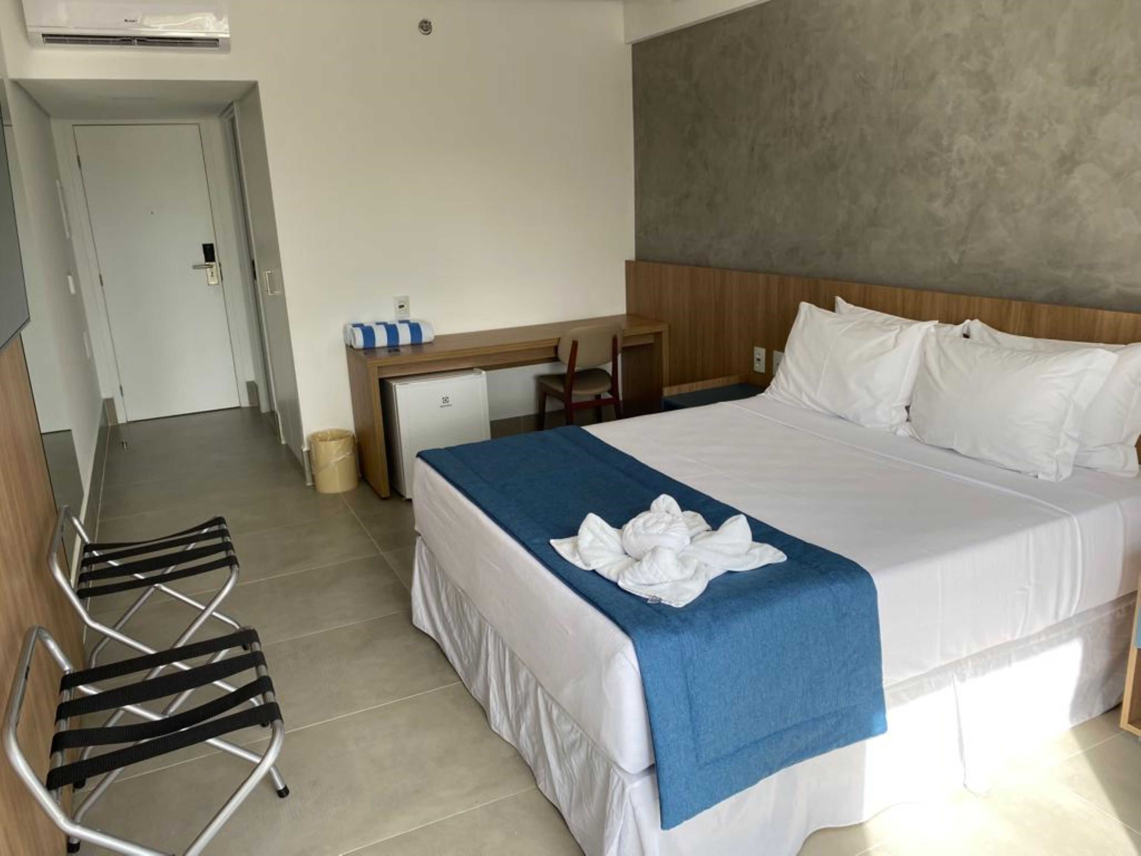 A hotel room with a bed, a desk, a chair, and a small refrigerator.