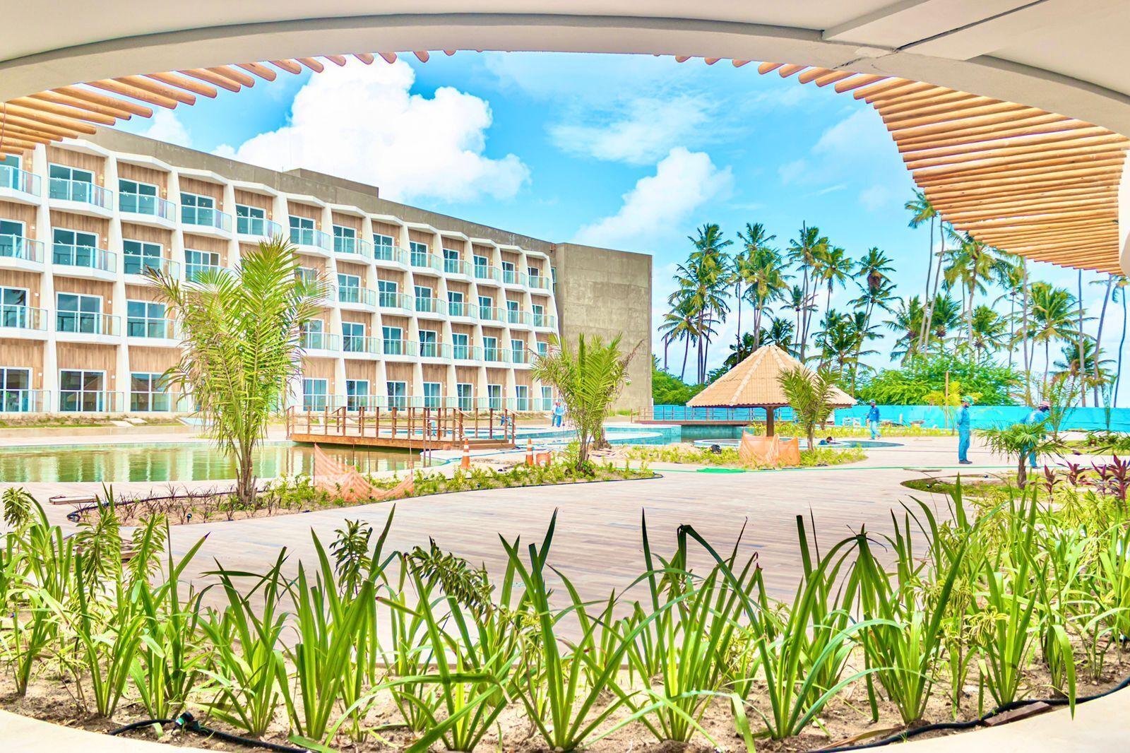 A hotel with a pool, palm trees, and a thatched-roof structure.