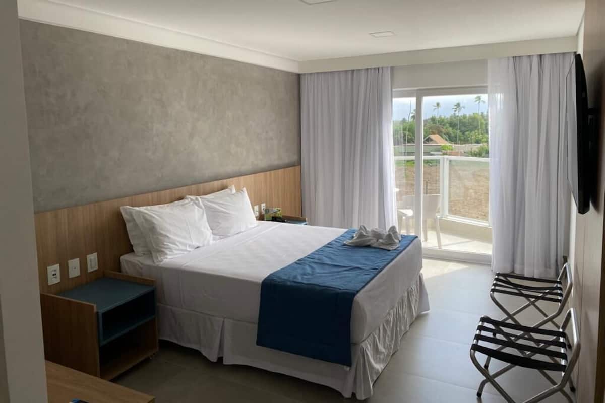 Een moderne hotelkamer met een groot bed, een klein bureau en een balkon met gordijnen.