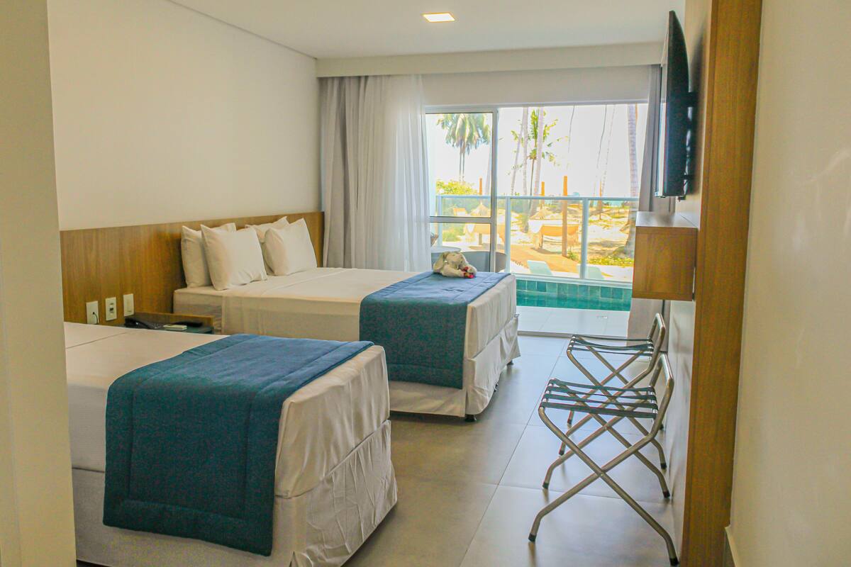 Een hotelkamer met twee bedden, een televisie en een balkon met uitzicht op palmbomen.