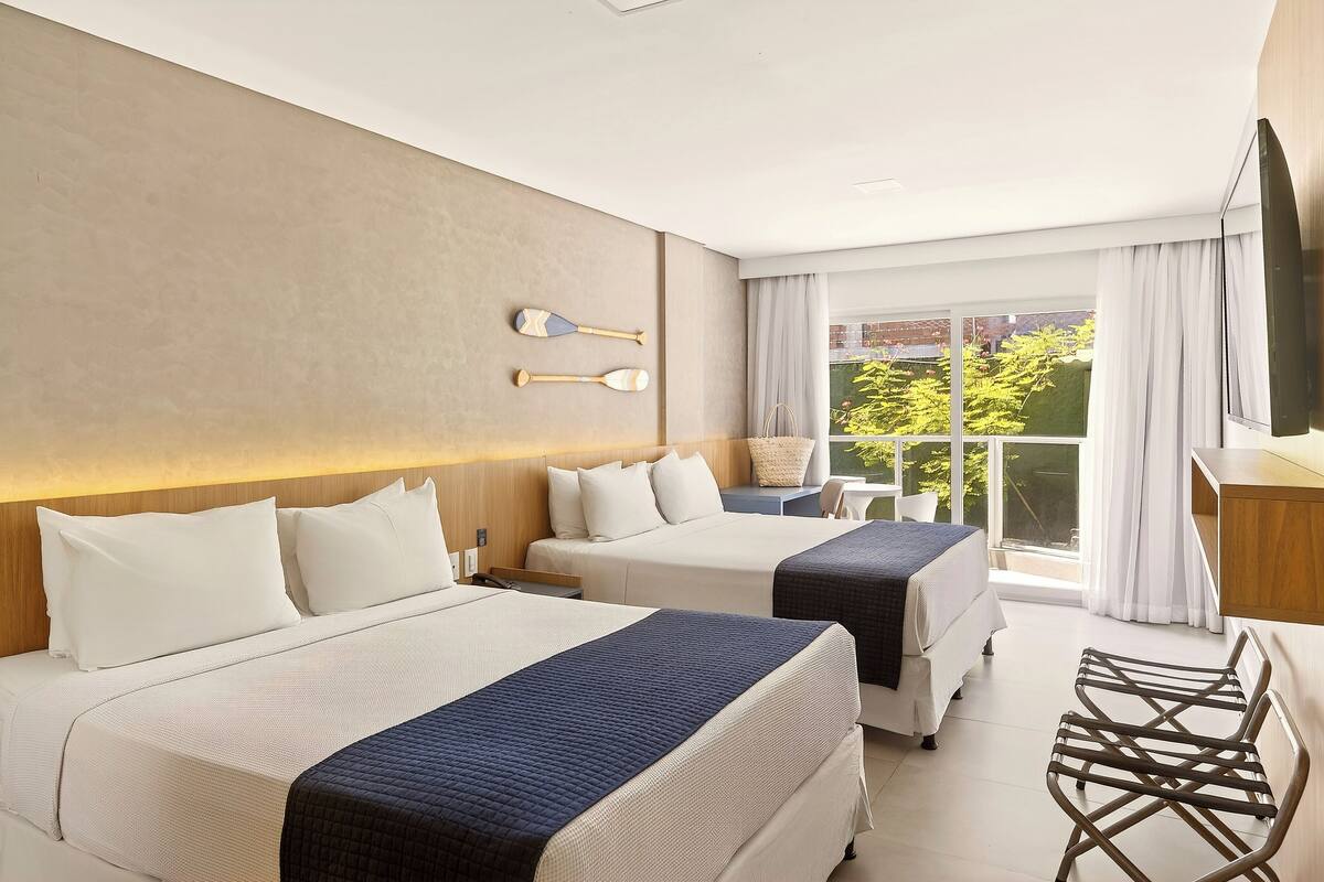 Een hotelkamer met twee bedden, een televisie, een bureau en uitzicht op groen.