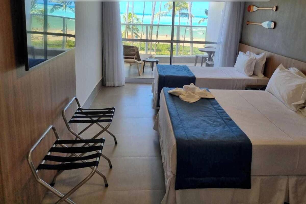 Een hotelkamer met twee bedden, een stoel en uitzicht op het strand.