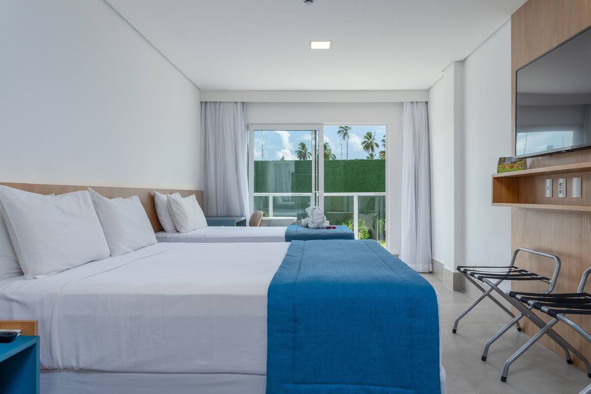 Een hotelkamer met twee bedden, een televisie, een bureau en uitzicht op palmbomen.