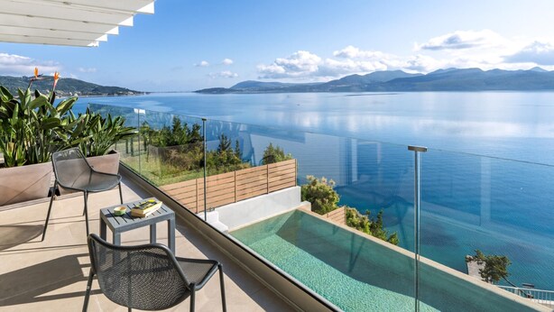 A balcony with a glass-bottomed infinity pool overlooking a calm sea and distant mountains.