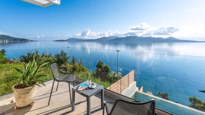 A balcony with a table and chairs overlooking a calm lake with mountains in the distance.