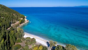 An aerial view of a coastal area with a beach, dense forest, and clear blue waters.