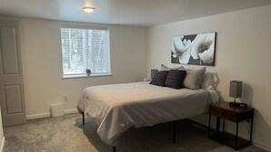 Une chambre à coucher comprenant un lit, une table de chevet, une lampe, une fenêtre et une œuvre d’art accrochée au mur.
