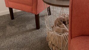 Une pièce avec un fauteuil rose, une table ronde et un panier en osier posé sur le sol.