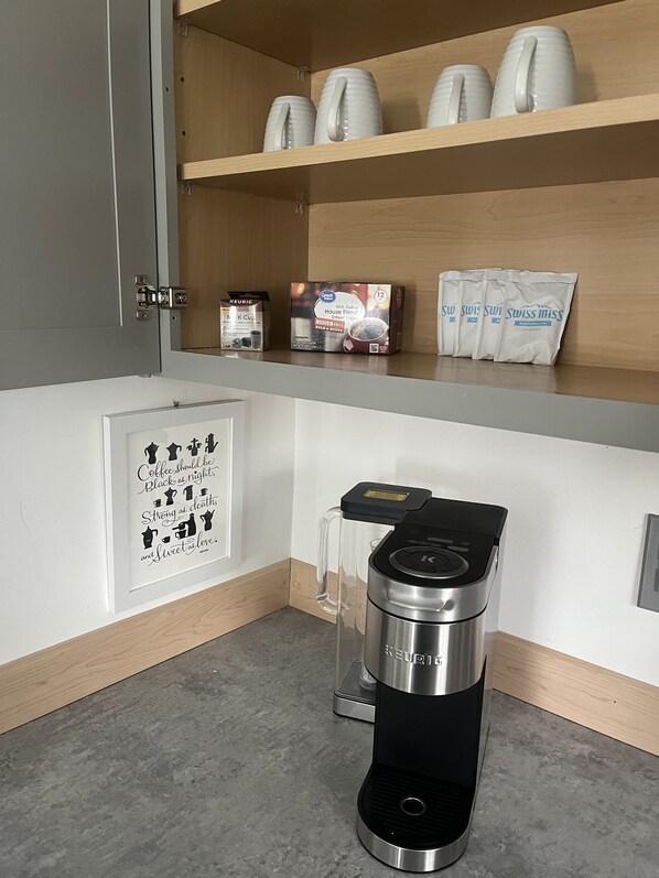 Una kitchenette con cafetera, una cita enmarcada y estantes con productos de café.