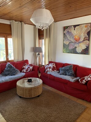 A cozy living room with a red sofa set, a round coffee table, and a large floral painting on the wall.