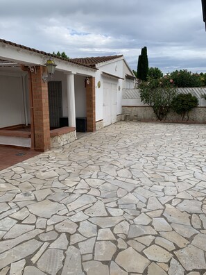 A courtyard with a stone floor, a covered entrance, and a white building with a tiled roof.