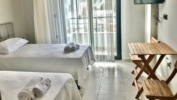 A hotel room with two beds, a TV, and a wooden table. - Liya Pansiyon (Ezine)