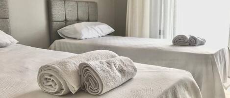 A hotel room with two beds, each with a headboard and a rolled towel on the bed.