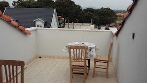 A small balcony with a table and two chairs, a tiled floor, and a view of neighboring buildings and trees. - Liya Pansiyon (Ezine)