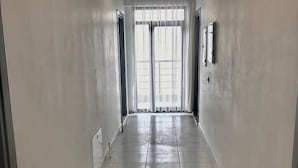 A hallway with tiled flooring, white walls, and a large window at the end. - Liya Pansiyon (Ezine)