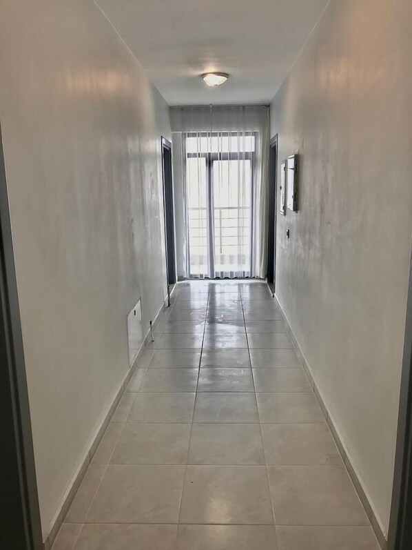 A hallway with tiled flooring, white walls, and a large window at the end. - Liya Pansiyon (Ezine)