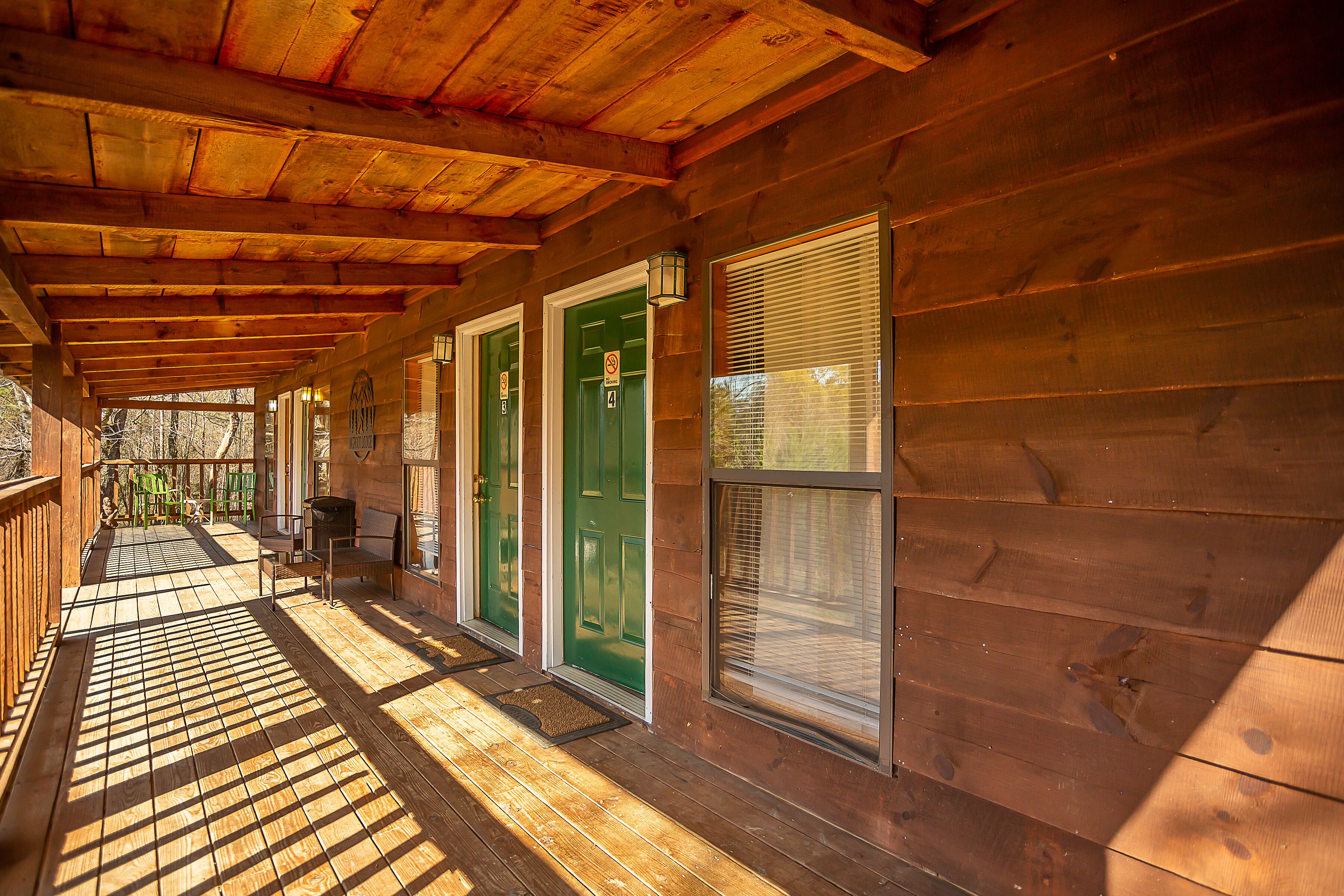 A wooden cabin with a covered porch, green doors, and a window with blinds.