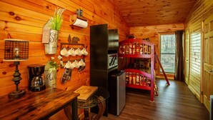 L’intérieur chaleureux d’un chalet avec des murs en bois, un plafond en bois, une petite table à manger, un réfrigérateur, une machine à café, une étagère avec des tasses et un lit superposé.