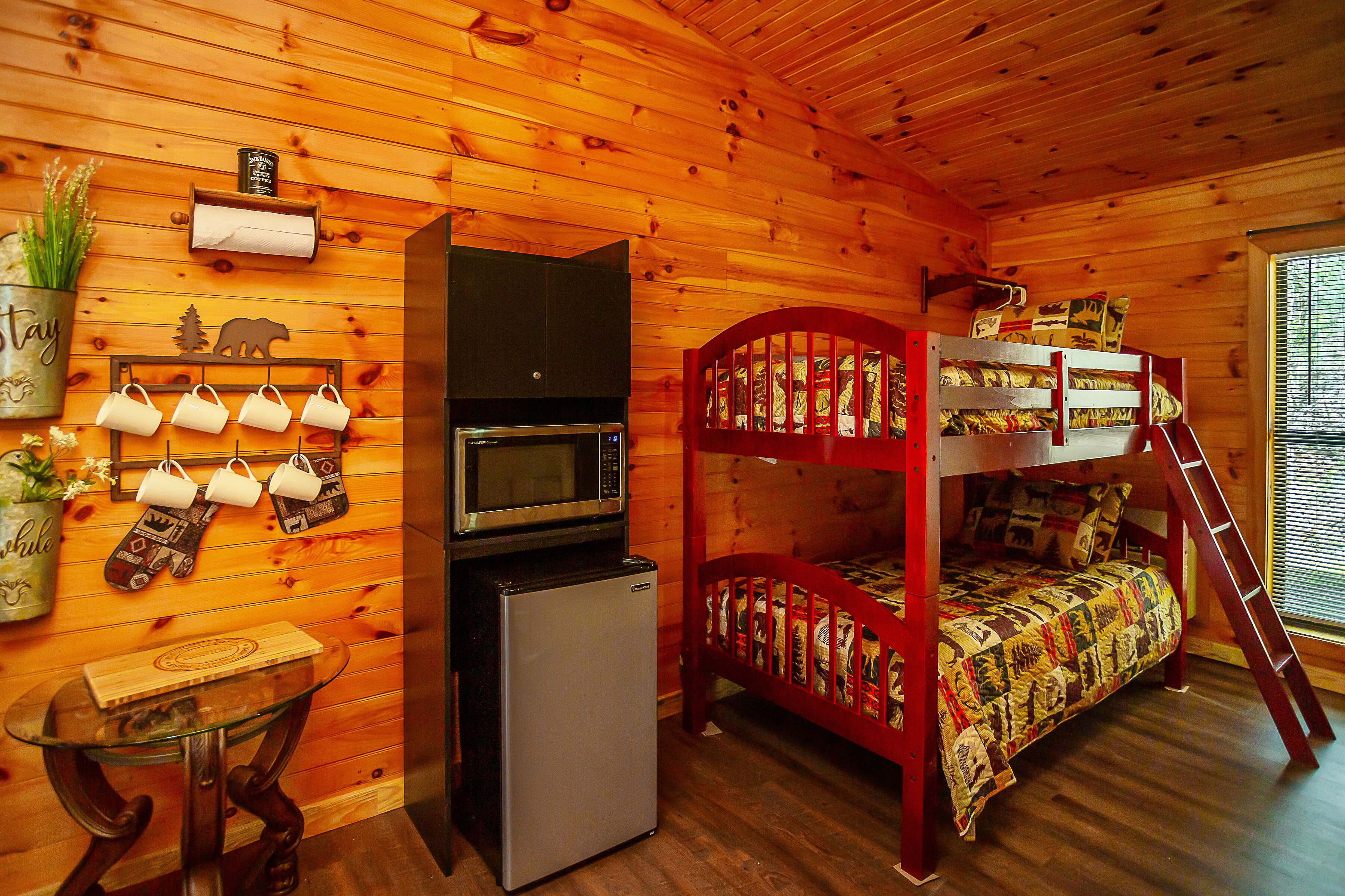 Une petite chambre comprenant un lit superposé, un réfrigérateur, un four à micro-ondes, une petite table et une étagère murale agrémentée d’une plante et d’une horloge.
