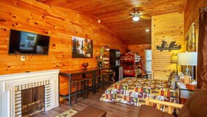 Une pièce aménagée dans le style d’un chalet en rondins, avec une cheminée, un lit recouvert d’une courtepointe, une télévision et un coin repas doté d’un bar.