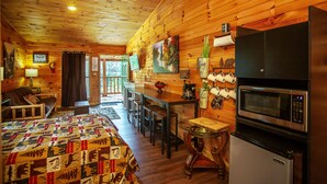 Un intérieur de chalet chaleureux avec un plafond en bois, un coin repas avec une table et des chaises, un lit avec une courtepointe et une cuisine équipée d’un four à micro-ondes et d’un réfrigérateur.