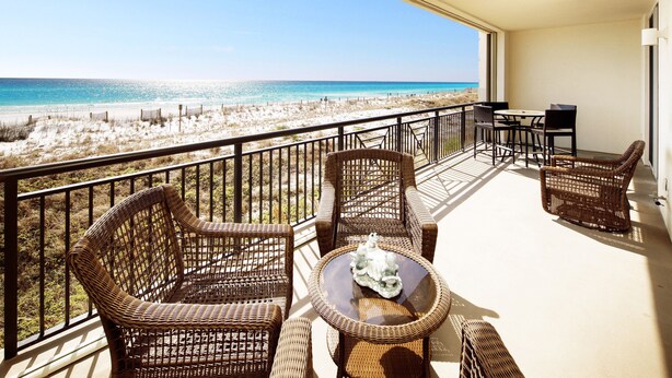 Ein Balkon mit Korbmöbeln, einem kleinen Tisch und Blick auf den Strand.
