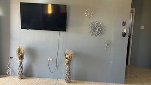A modern living room with a flat-screen TV mounted on the wall, decorative wall art, and two vases with dried flowers on the floor. - Williams Oasis (Falmouth)