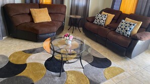 A living room with two brown sofas, a glass coffee table, and a patterned rug. - Williams Oasis (Falmouth)