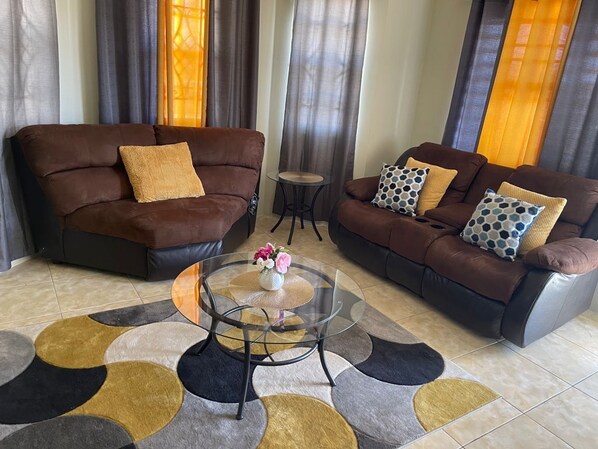A living room with two brown sofas, a glass coffee table, and a patterned rug.