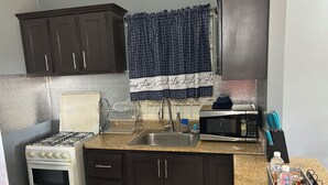 A kitchen with dark cabinets, a white stove, a microwave, and a sink. - Williams Oasis (Falmouth)