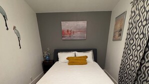 Un dormitorio con cama, mesita de noche, un jarrón con flores y un cuadro en la pared.