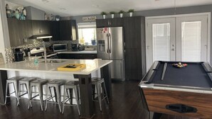 Una cocina moderna con una isla central, taburetes de bar, mesa de billar y ventilador de techo.