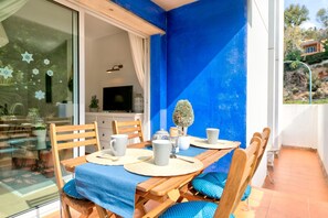 Comedor con mesa de madera dispuesta para cuatro personas, televisor al fondo y pared azul.