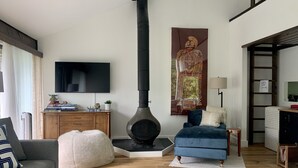 Een woonkamer met een grote, zwarte houtkachel, een blauwe bank, een grijze bank, een flatscreen televisie en een groot decoratief schilderij.