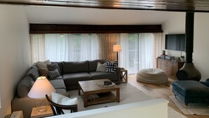 Een gezellige woonkamer met een hoekbank, een salontafel, een houten vloer, een televisie en een open haard.