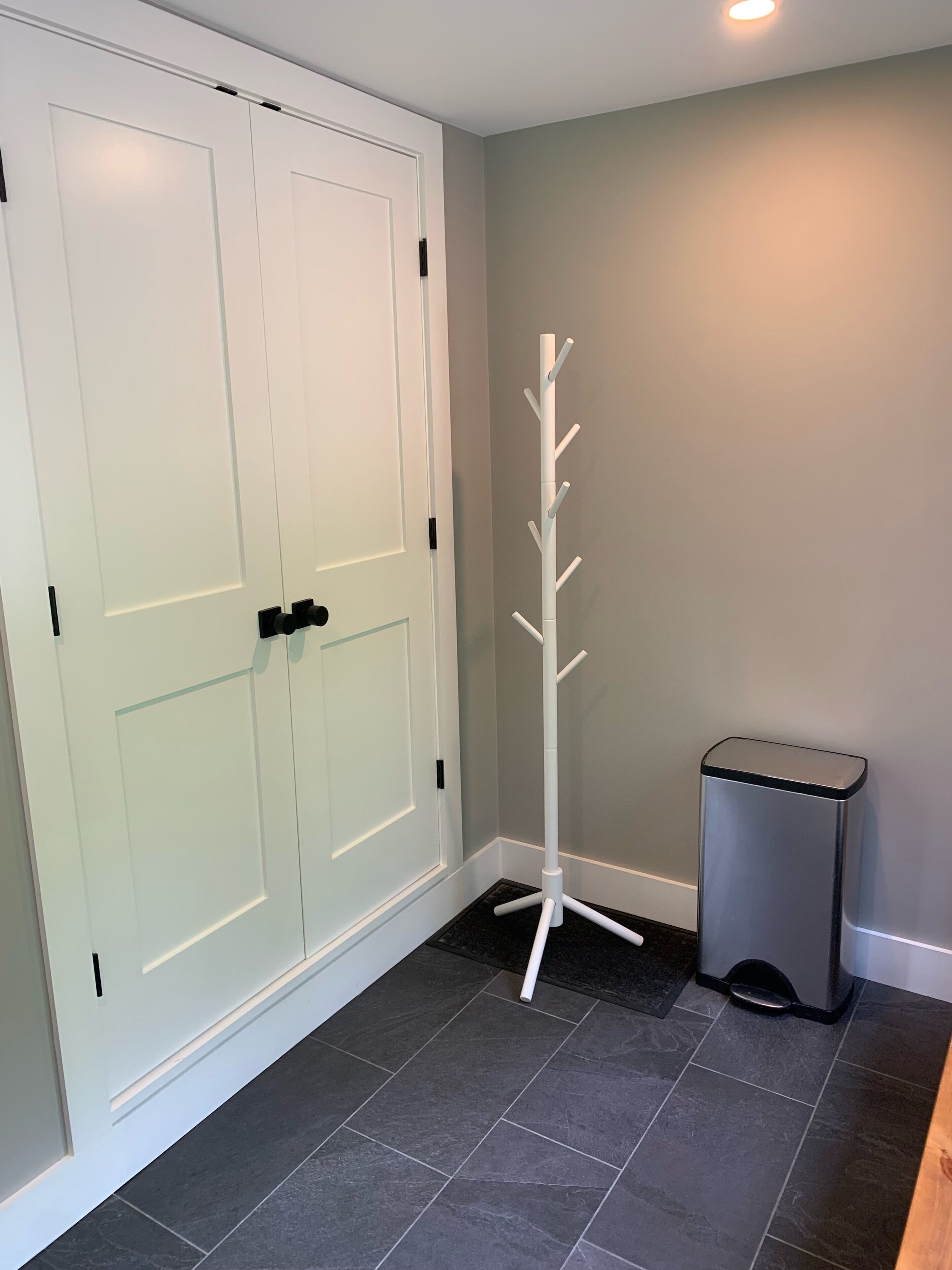 A room with a white door, a coat rack, and a trash bin.