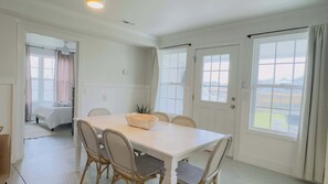 A room with a white table, wicker chairs, a bed, and large windows. - Murrells inlets #A Great duplex walk to the beach (Murrells Inlet)