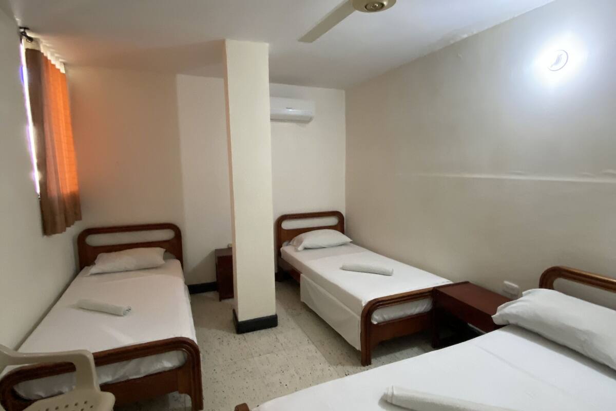 Una habitación con tres camas individuales, ventilador de techo, aire acondicionado y una silla blanca.