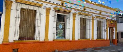 Fachada de hotel con ventanas protegidas por barrotes, revestimiento amarillo y blanco, y un letrero que indica que es un hotel.